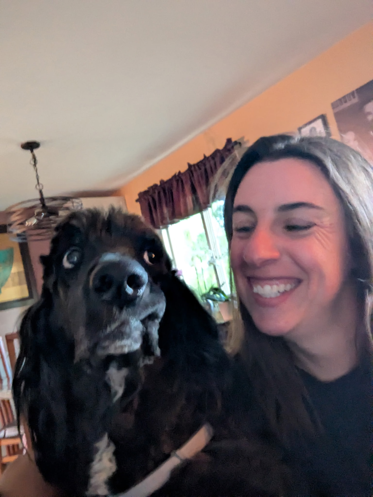 Sarah laughing beside a black spaniel mix during a drop-in visit